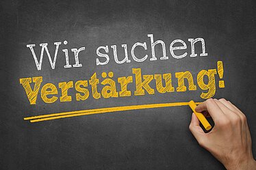 Wir suchen Verstärkung! Hand schreibt mit Kreide Text "Wir suchen Verstärkung!" auf Tafel